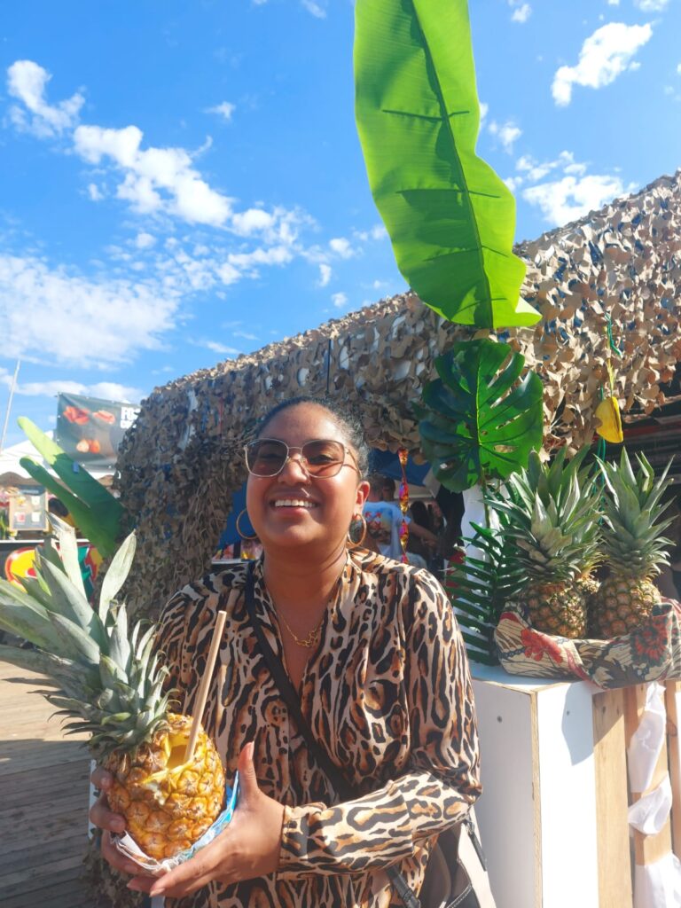 Fariel Soeleiman houdt een ananas met een rietje erin, heeft een tijgerprint blouse aan en staat lachend buiten op het KWAKU festival.